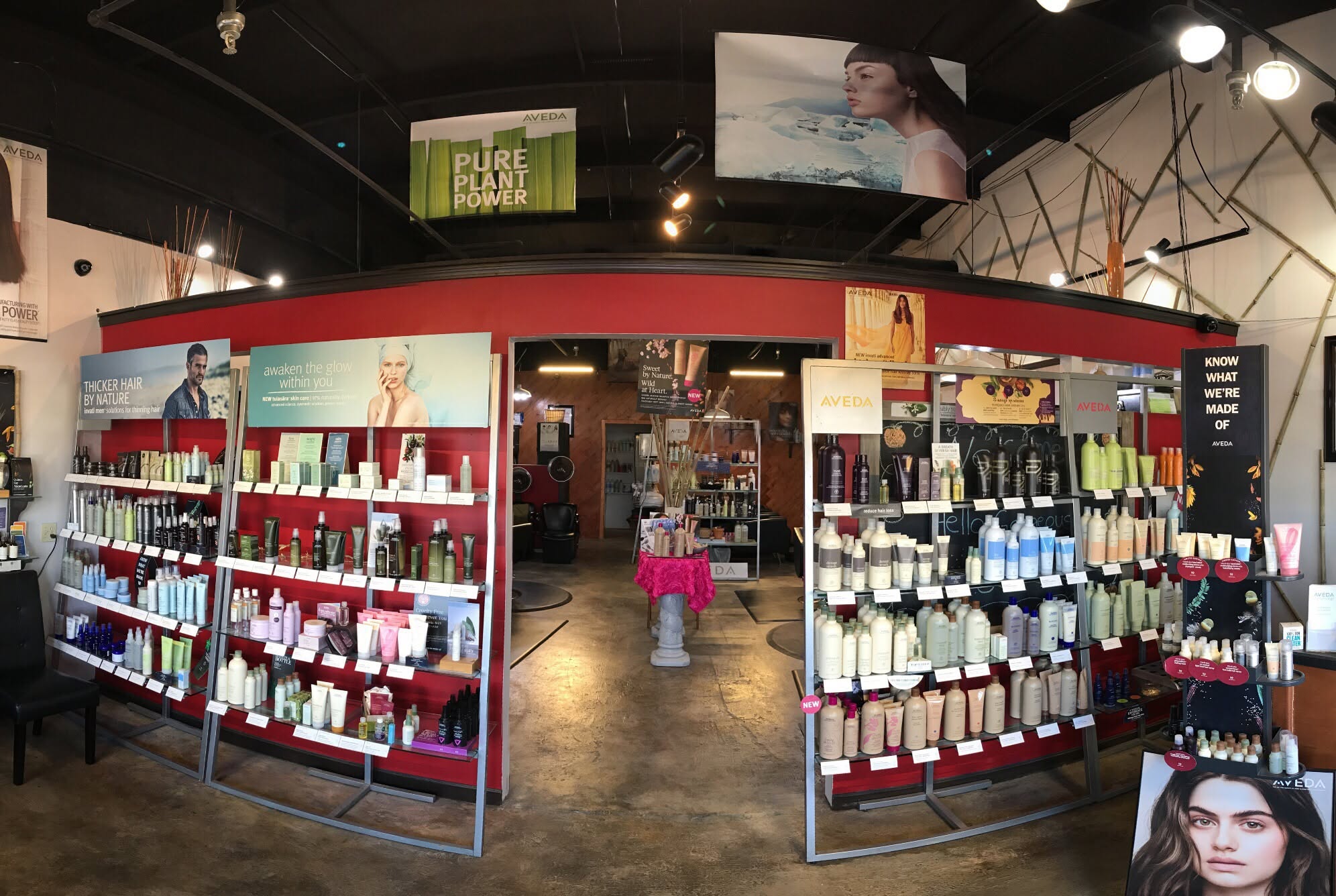 A beauty expo booth displays skincare and makeup on metal shelves, with red walls and product posters creating a colorful, busy retail feel.