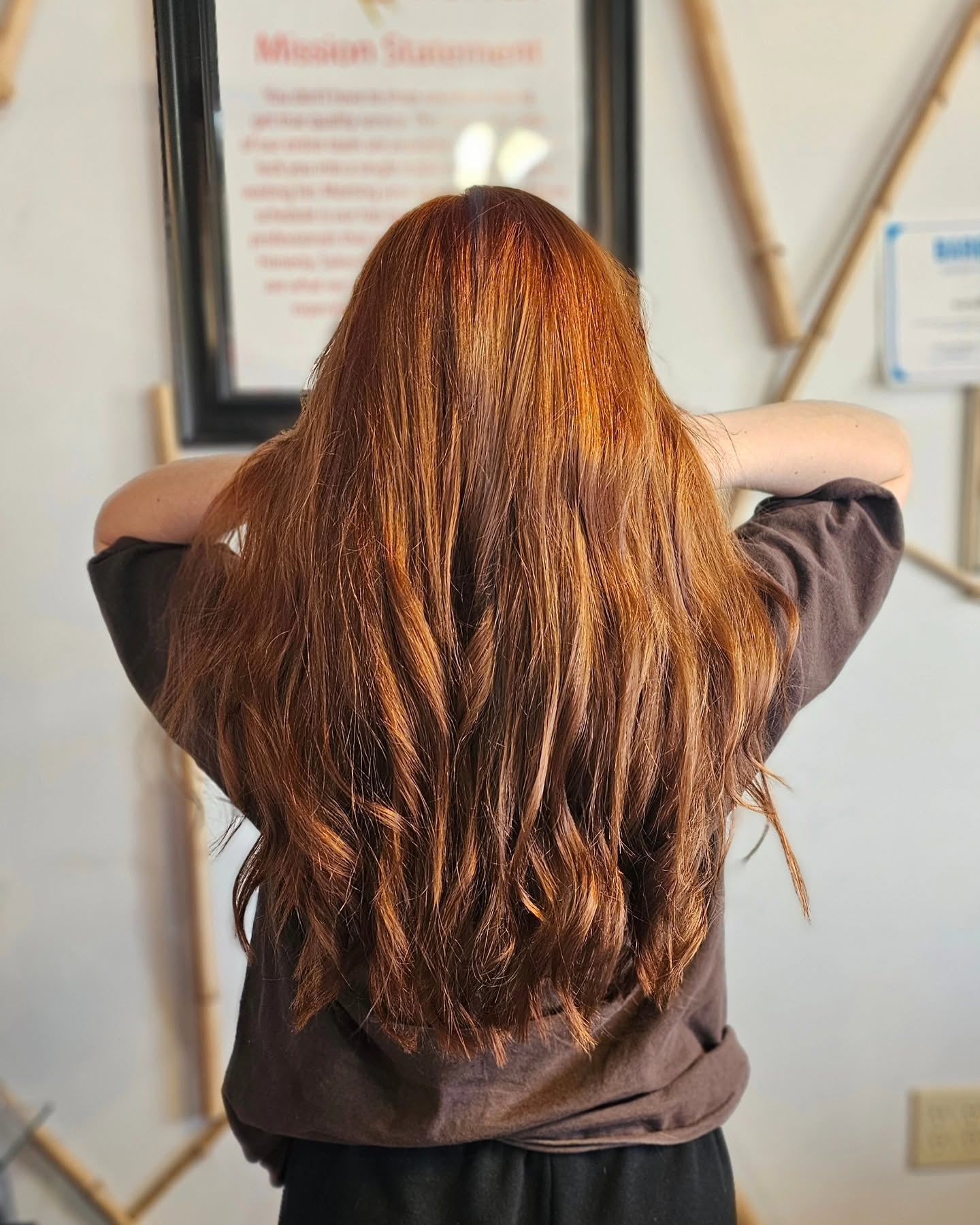 A person with long, wavy auburn hair stands with their back to the camera, arms raised toward a framed museum statement; the scene feels calm and reflective.