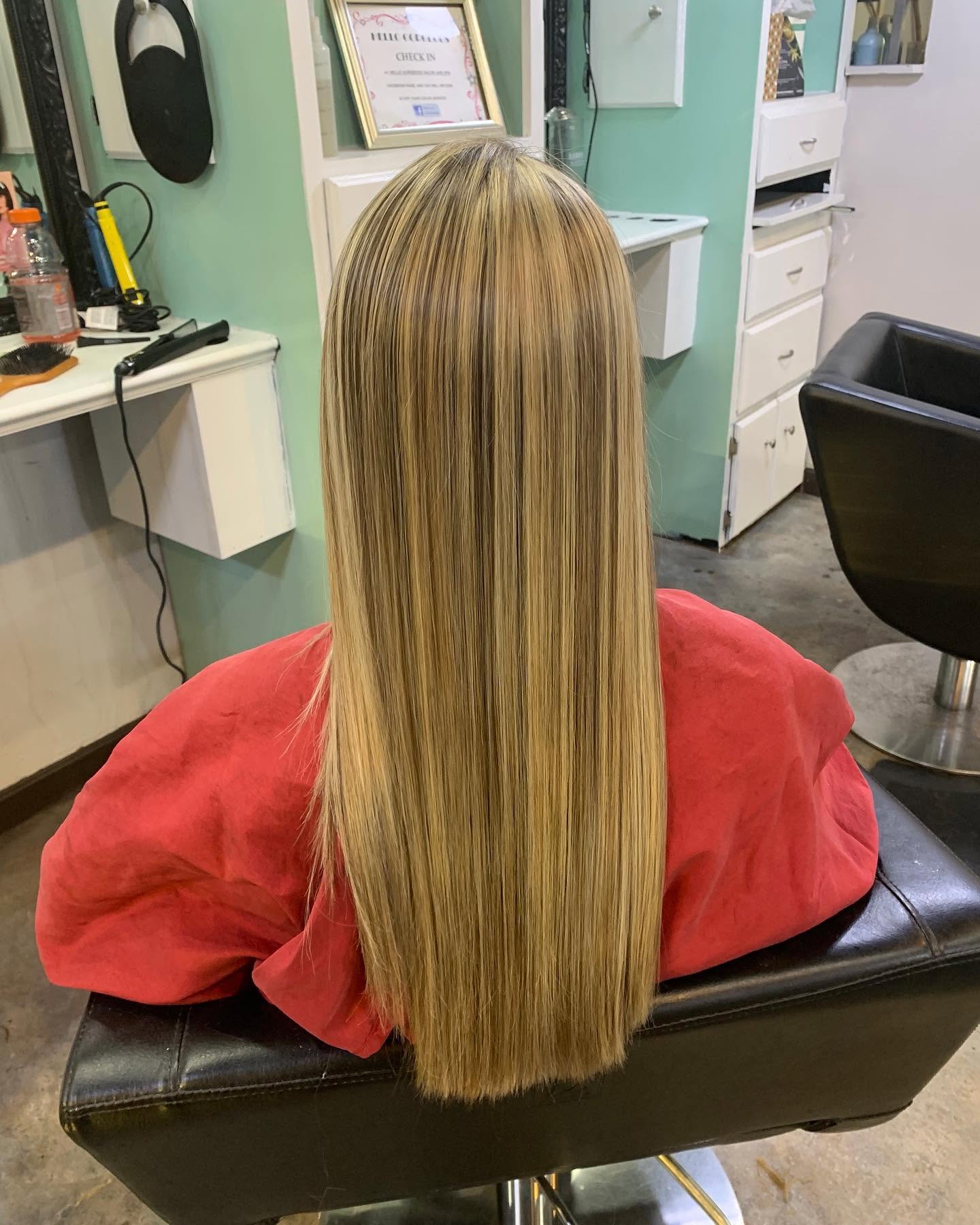 Back view of a salon client in a red cape, with long, straight, glossy blonde hair and fine highlights falling neatly down her back.